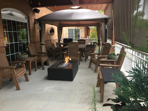 A cozy outdoor patio setup featuring wooden chairs, a modern fire pit, and a protective canopy for comfortable gatherings.