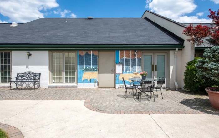 A small building with a patio featuring a table and chairs, under a clear blue sky.