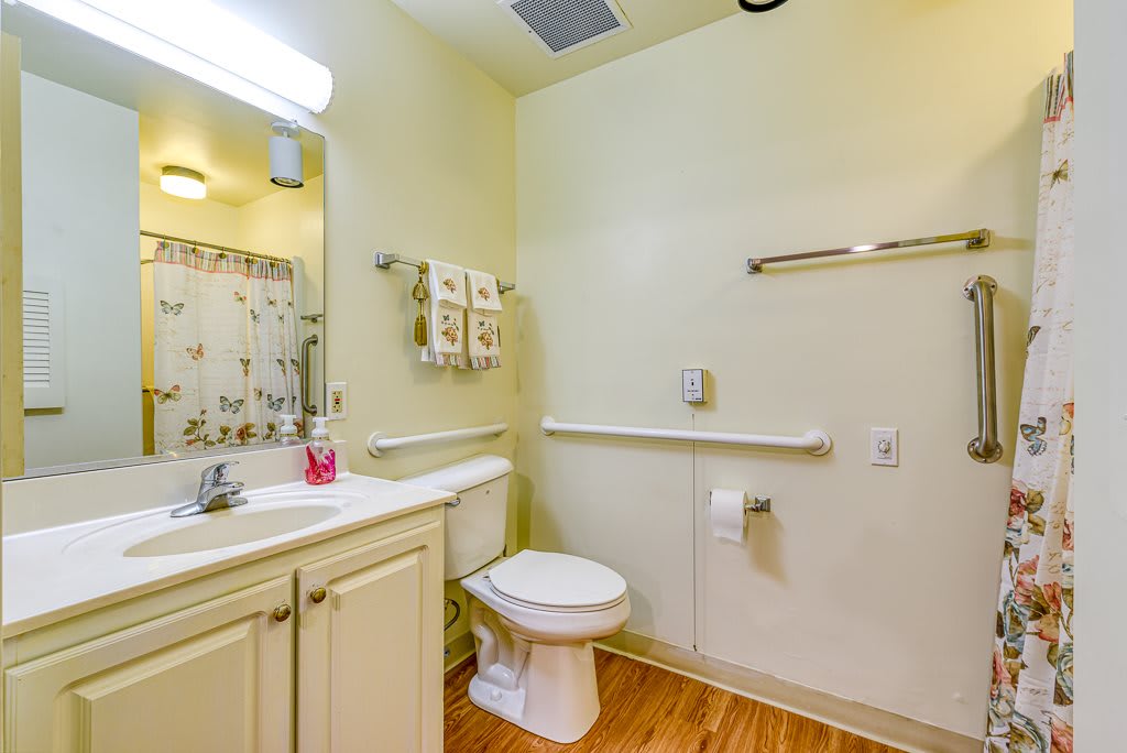 A well-lit bathroom featuring a toilet, sink with mirror, and shower curtain.