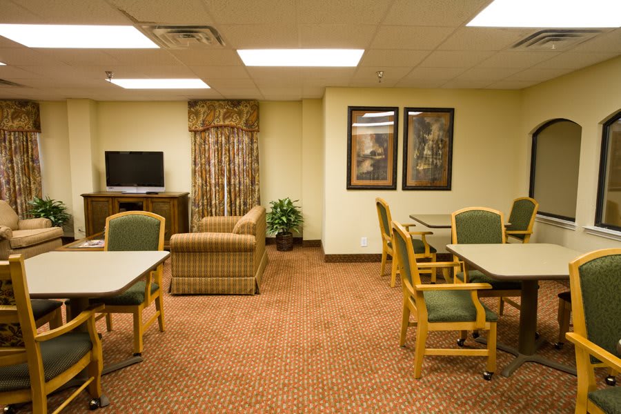 A lounge area featuring multiple tables and chairs, with a sofa and television in the background.