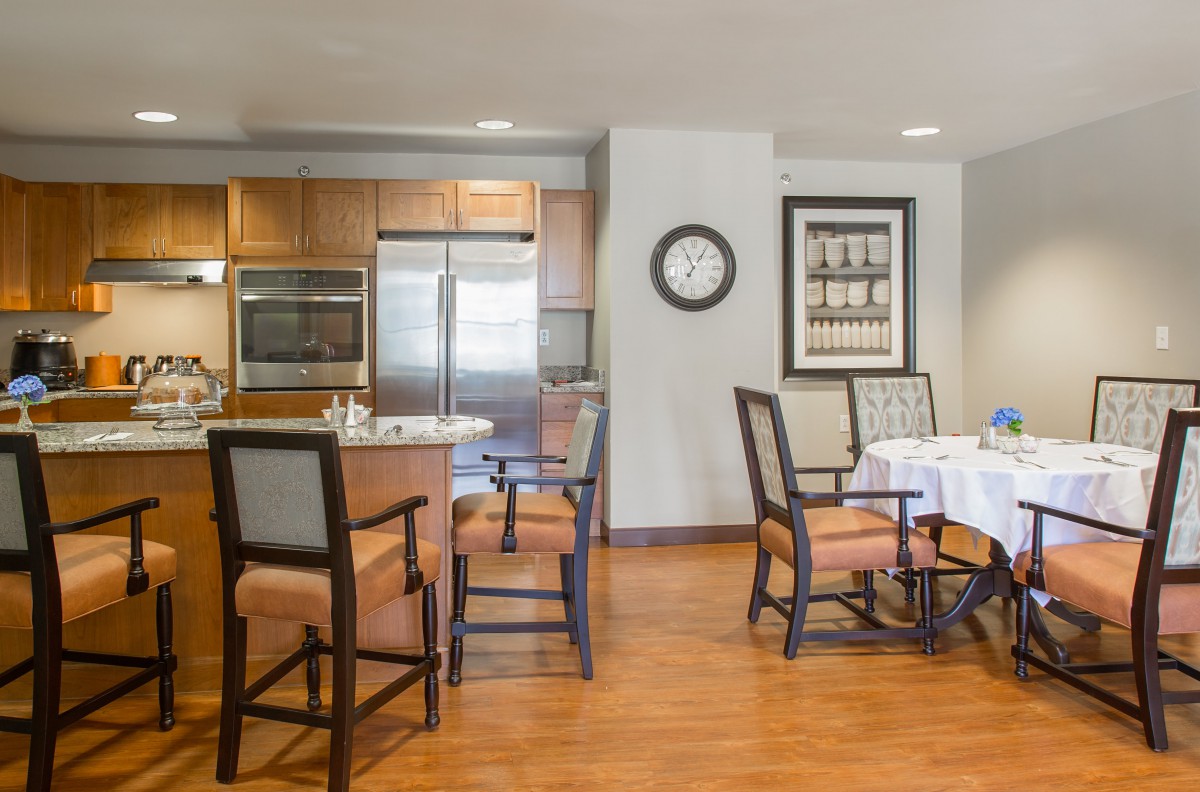 A modern kitchen and dining area with wooden flooring, featuring a countertop, chairs, and dining table.