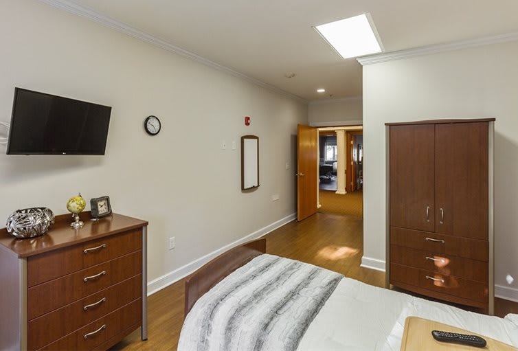 A well-lit bedroom with a bed, dresser, and television on the wall.