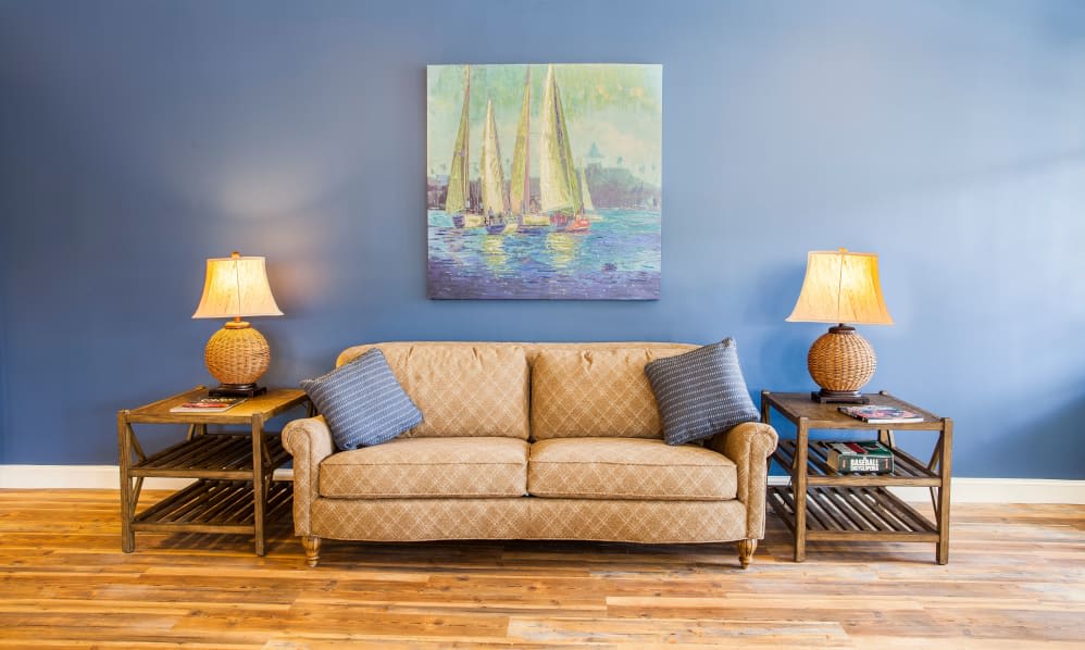 A cozy living room with a beige sofa, blue pillows, and a nautical-themed painting on the wall.