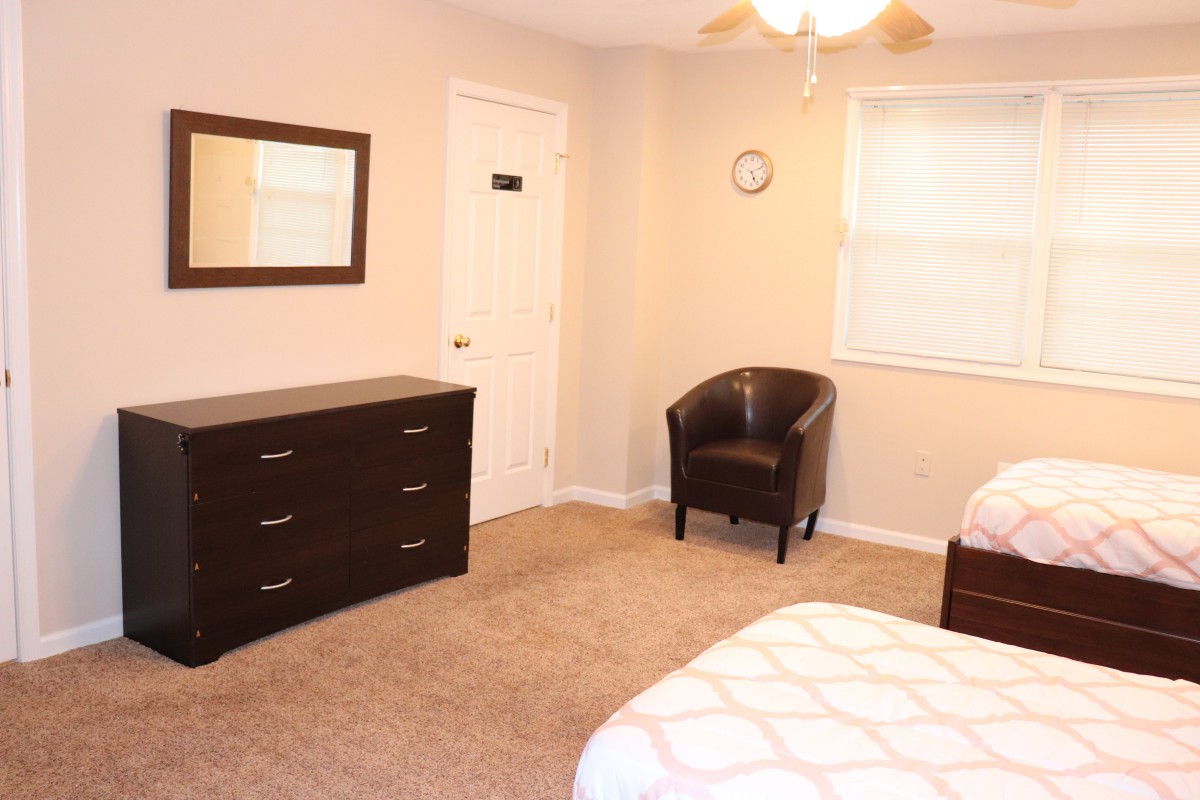 A tidy bedroom featuring a bed, dresser, mirror, and chair with neutral-colored walls.