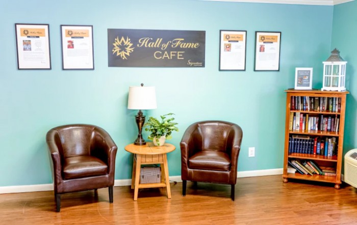 A cozy cafe waiting area with leather chairs, a lamp, and framed decorations on the wall.