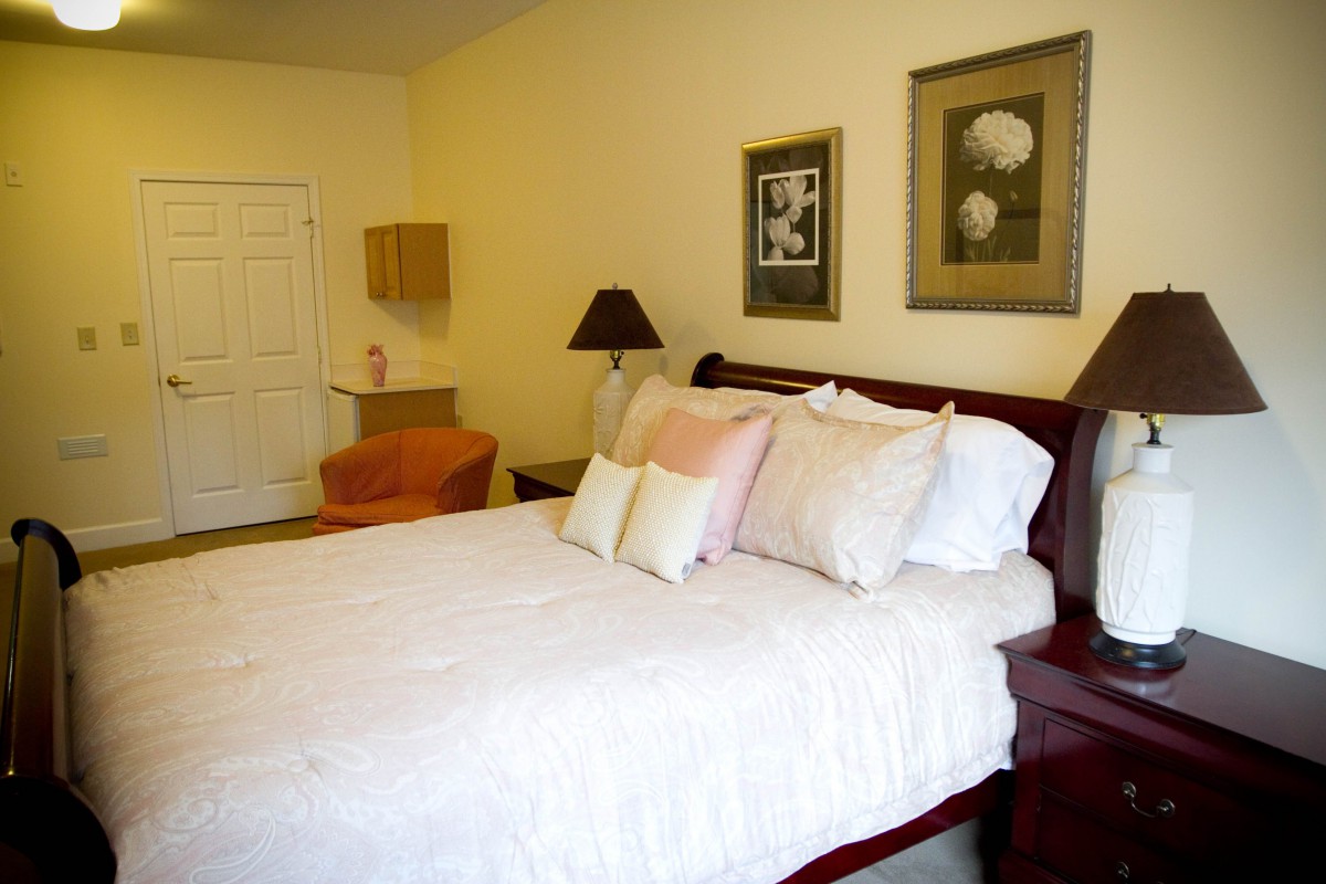 A cozy bedroom interior featuring a neatly made bed, wall art, and a lamp.
