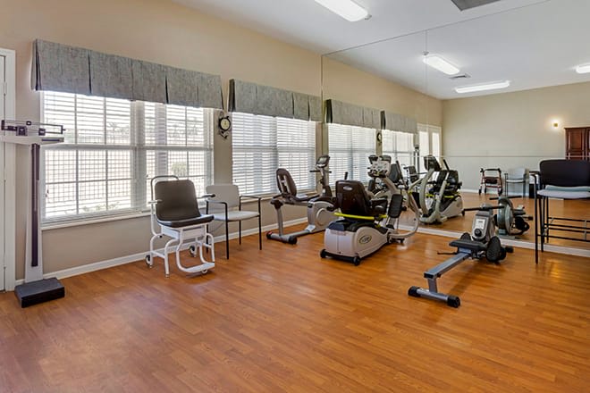 An indoor gym with various exercise equipment and wooden flooring.
