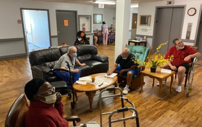 A group of elderly individuals socializing in a community center setting, sitting on couches and chairs.