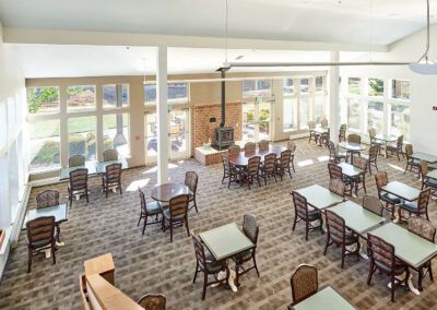 A bright, spacious dining area with multiple tables and chairs, featuring large windows that let in natural light.