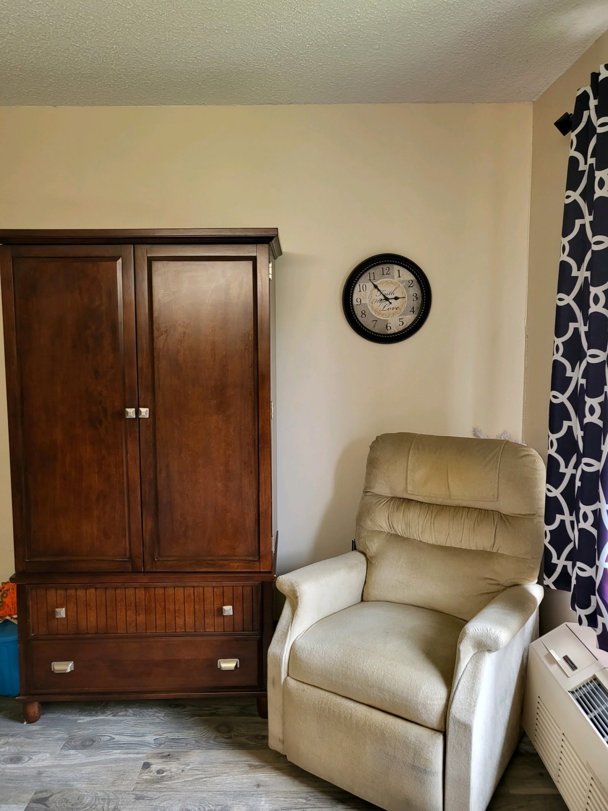 A cozy room with a recliner chair, wooden cabinet, and wall clock.