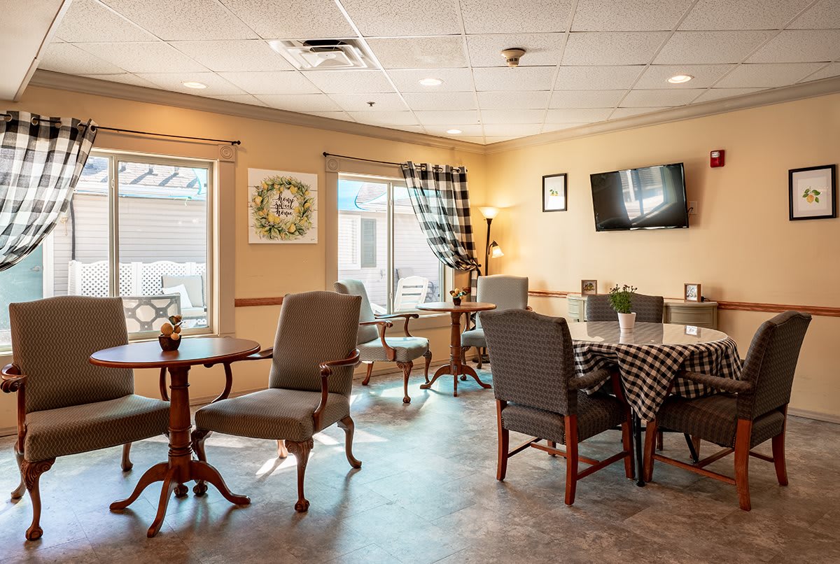 A cozy dining area with tables, chairs, and a wall-mounted television, featuring soft lighting and checkered curtains.
