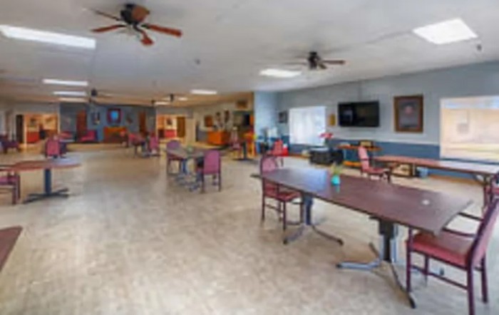 A spacious indoor room featuring tables, chairs, ceiling fans, and a television.