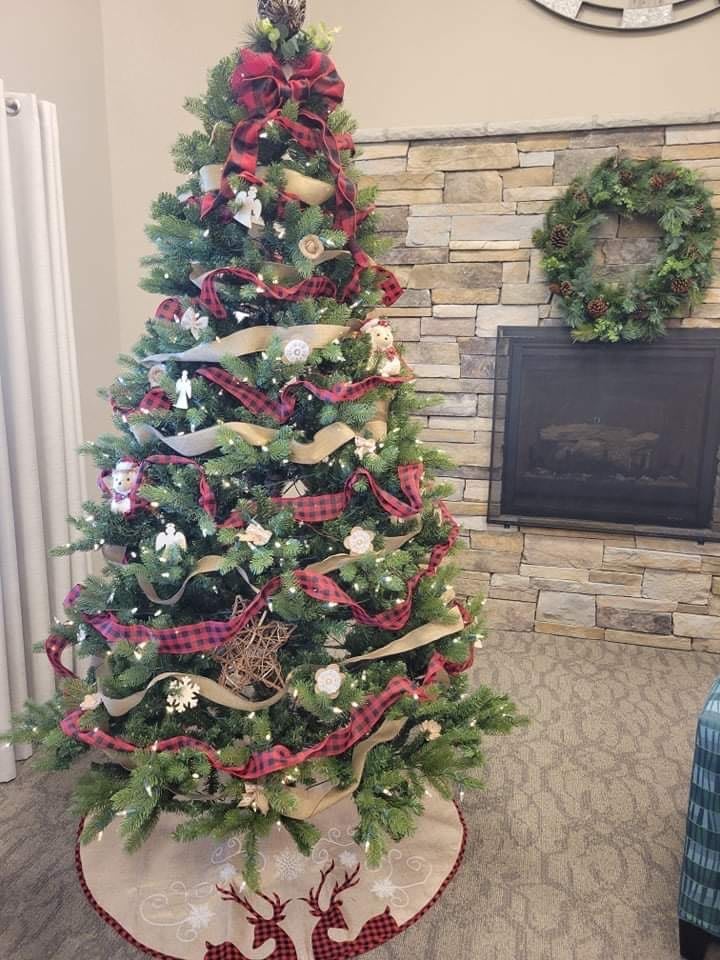 A beautifully decorated Christmas tree with ribbons, ornaments, and a wreath near a cozy fireplace.