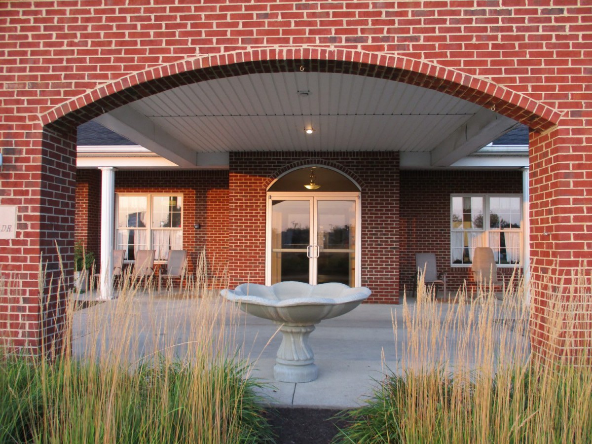 An elegant brick building entrance with a central fountain surrounded by tall grasses.