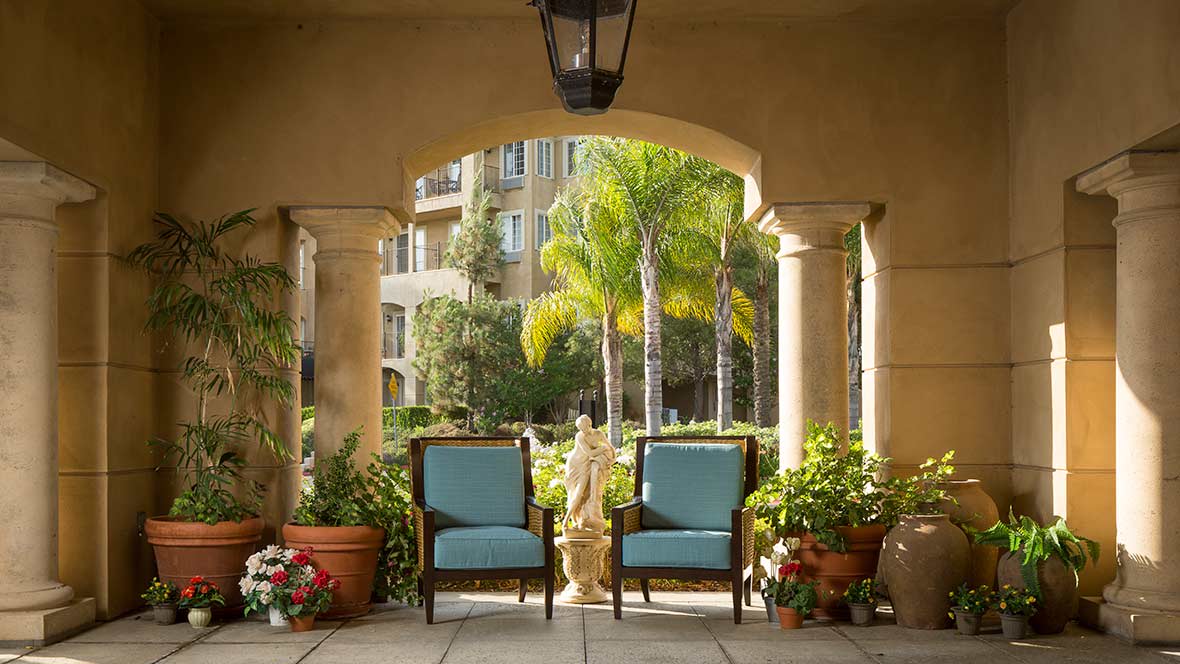 A serene patio area with two chairs and lush greenery under an archway.