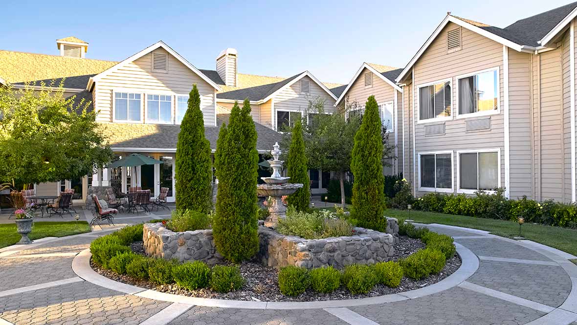 A beautifully landscaped residential building with a central fountain surrounded by trees.