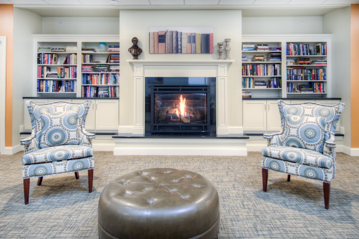 A cozy library with a fireplace, surrounded by bookshelves and comfortable seating.