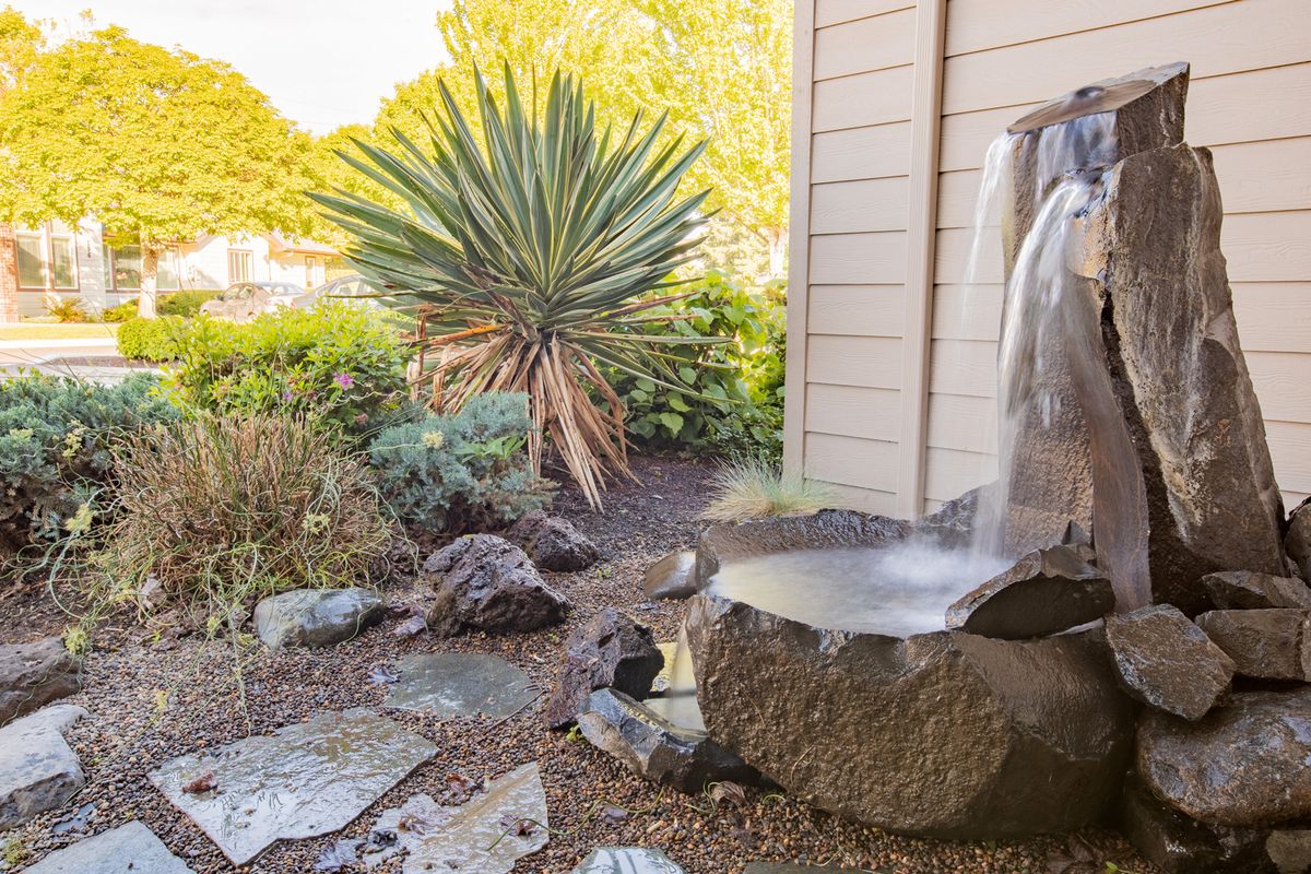 A serene garden space featuring a small water fountain, surrounded by lush greenery and rocks.