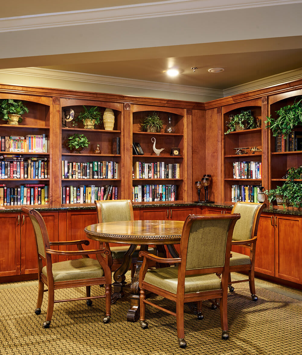 A cozy library corner with wooden bookshelves, a round table, and chairs for reading.
