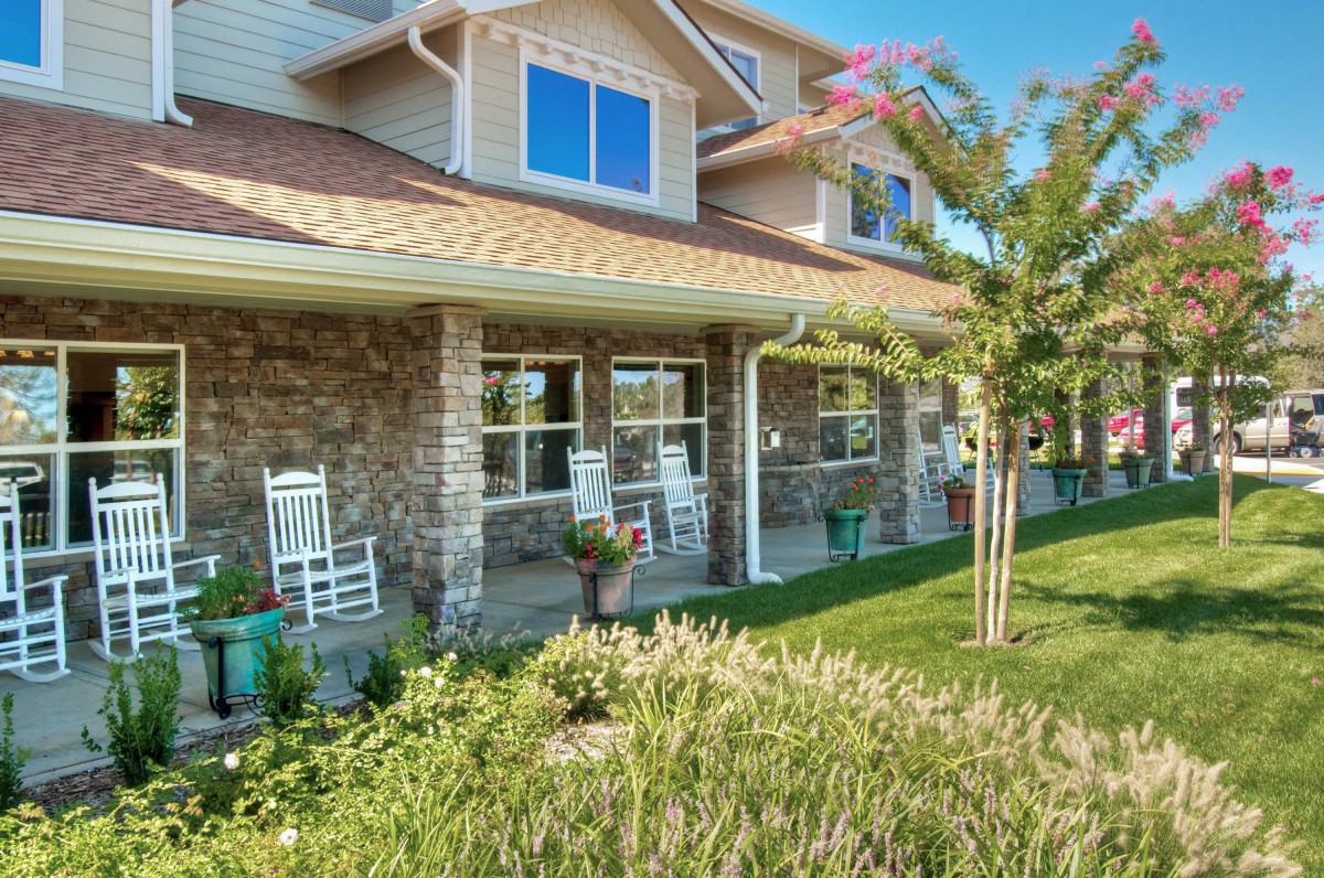A charming house with a stone exterior features a cozy porch equipped with white rocking chairs, surrounded by a well-maintained garden.