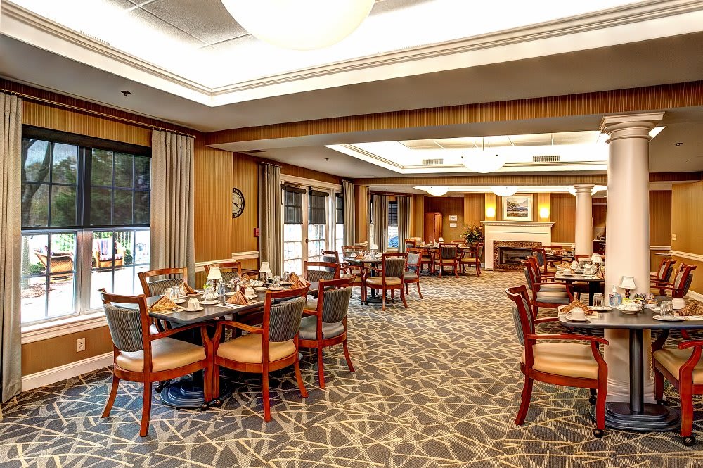 An elegantly designed restaurant dining area with neatly arranged tables and chairs, featuring warm lighting and carpeted floors.
