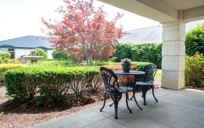 A cozy patio with a table and chairs overlooking a garden with vibrant foliage.