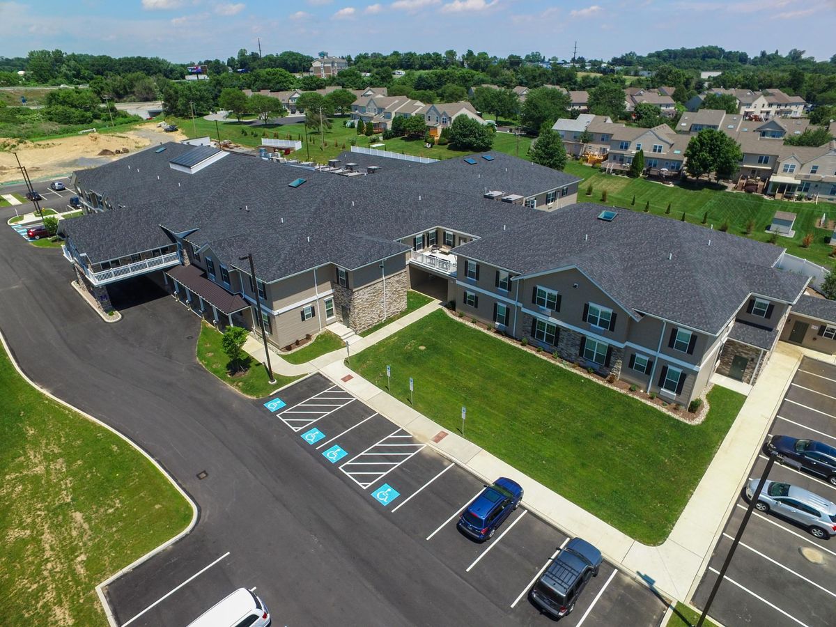 Aerial view of a large building with a parking lot surrounded by greenery in a residential area.
