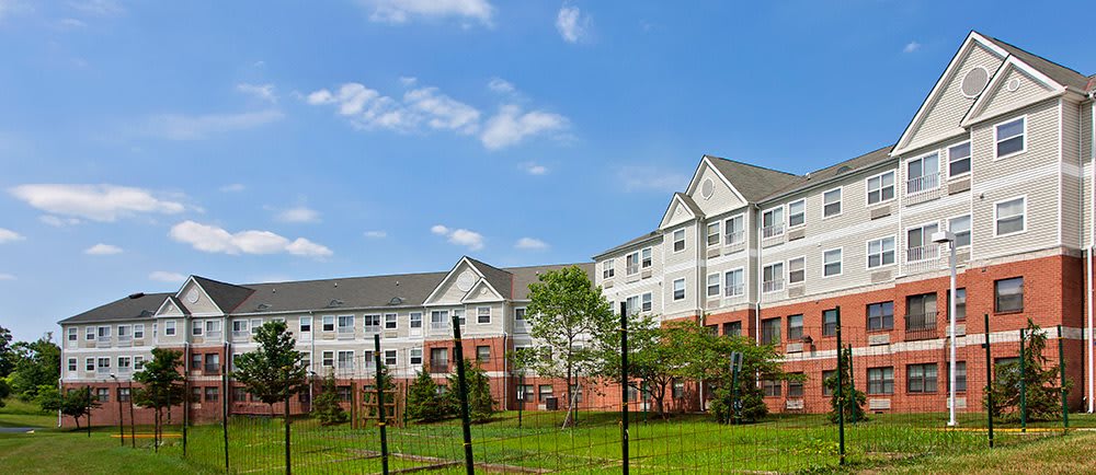 A residential apartment building with a well-kept lawn and surrounding trees under a clear blue sky.