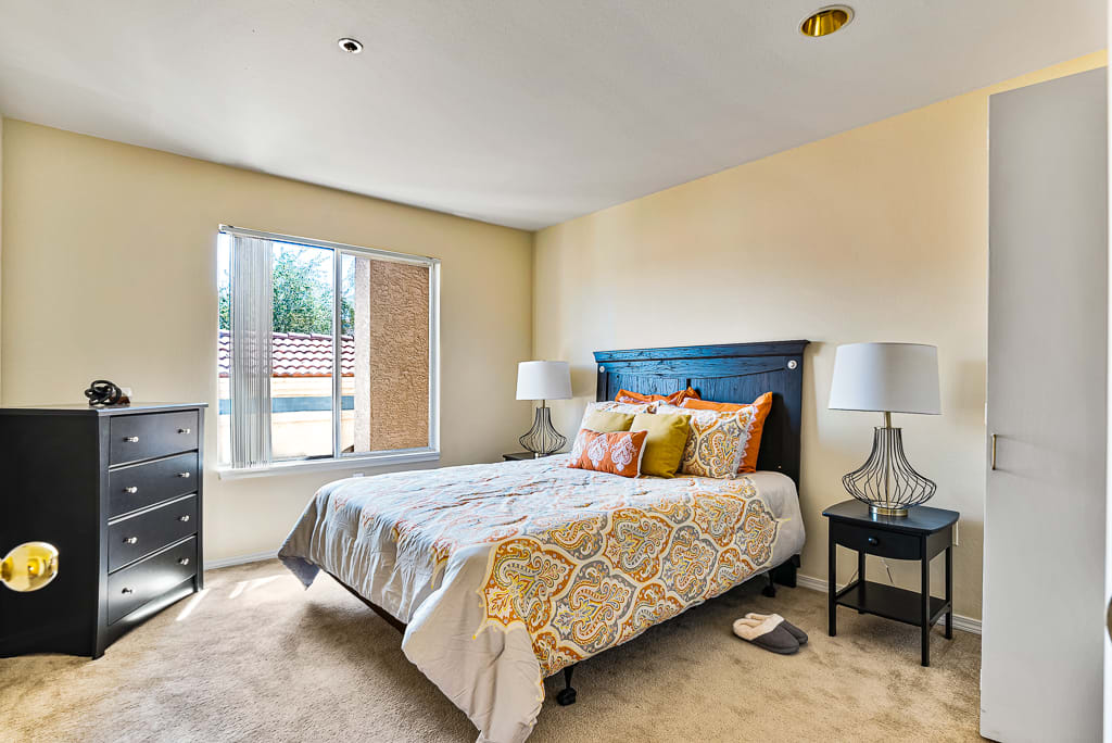 A modern bedroom with a neatly made bed, colorful pillows, and ample natural light streaming through the window.