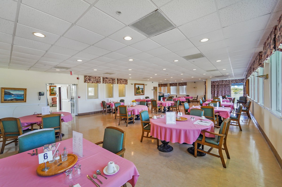 A spacious dining room with multiple tables covered in pink tablecloths, set for guests.