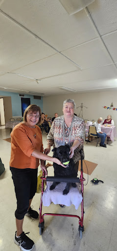 Two women pose with a dog during a community gathering.
