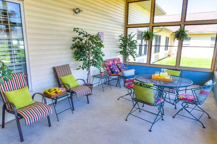 A cozy patio area with colorful cushioned chairs and a table, surrounded by lush green plants.