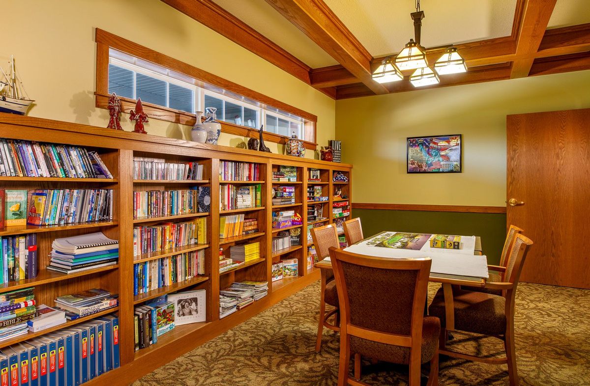 A cozy library room with wooden bookshelves filled with books and a central table surrounded by chairs.