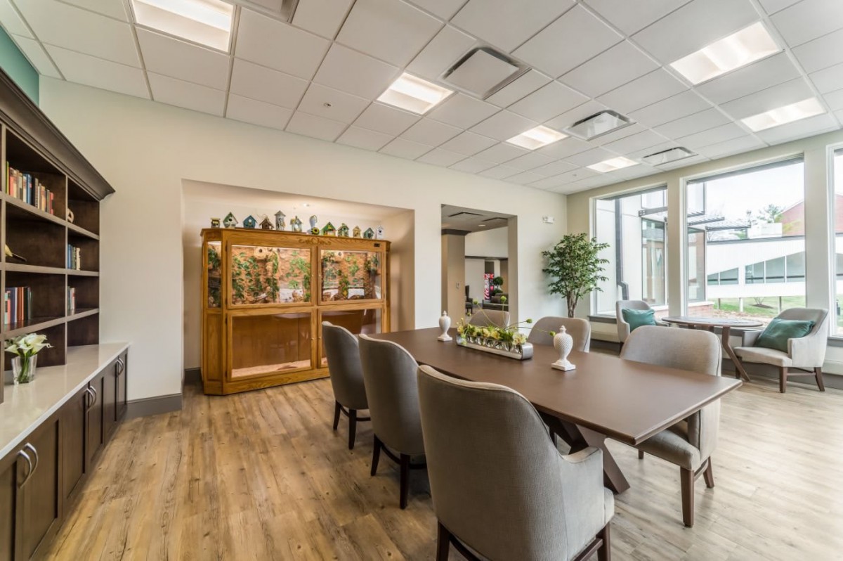 A modern meeting room with a large conference table, chairs, and decorative cabinet under natural lighting.