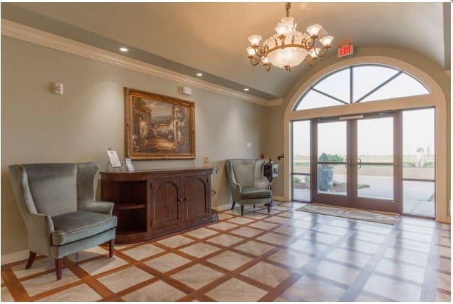 A stylish lobby featuring elegant armchairs, a chandelier, and a large window allowing natural light to fill the space.