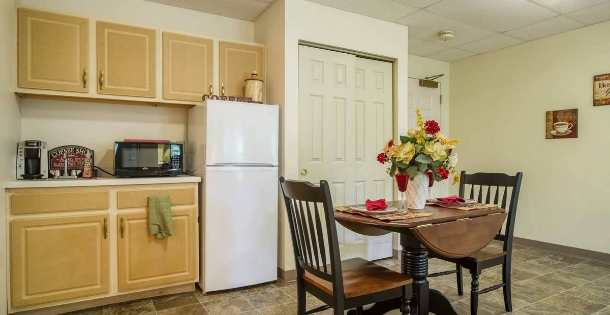 A cozy kitchen and dining area featuring a table with flowers, chairs, a refrigerator, cabinets, and a microwave.