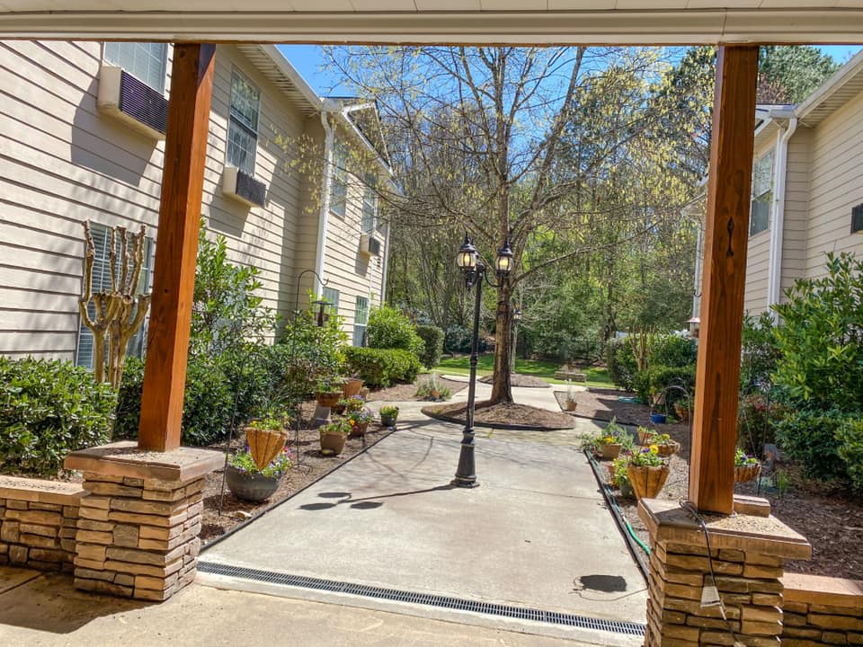 A serene garden pathway bordered by trees and plants leading to residential buildings.