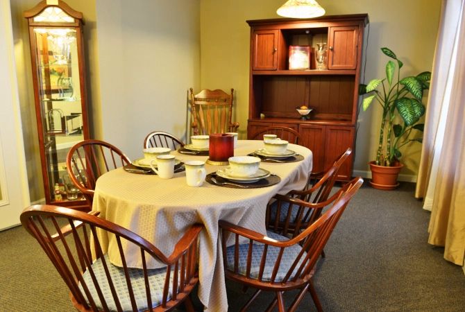 A dining room featuring a table set for four with wooden chairs and a cabinet in the background.