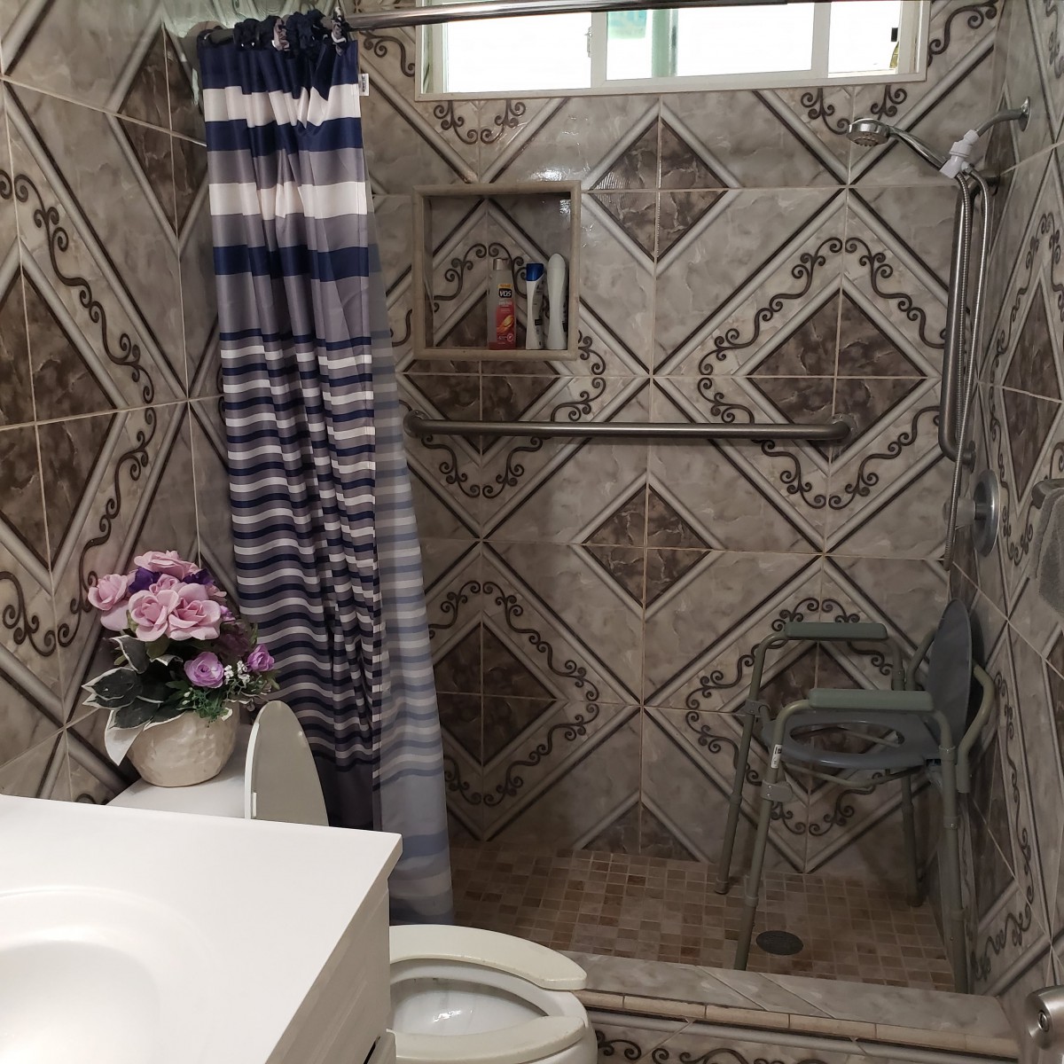 A tiled bathroom with a shower area, curtain, toilet, and decorative flowers.
