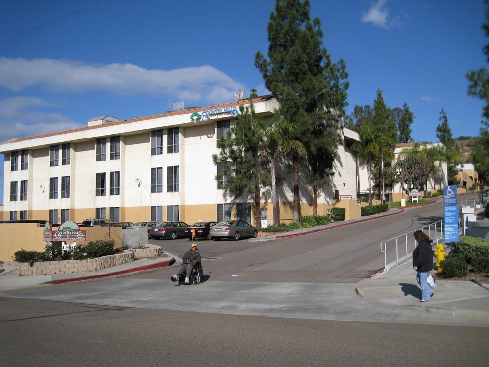 A view of a residential apartment building with people on the sidewalk and trees nearby.