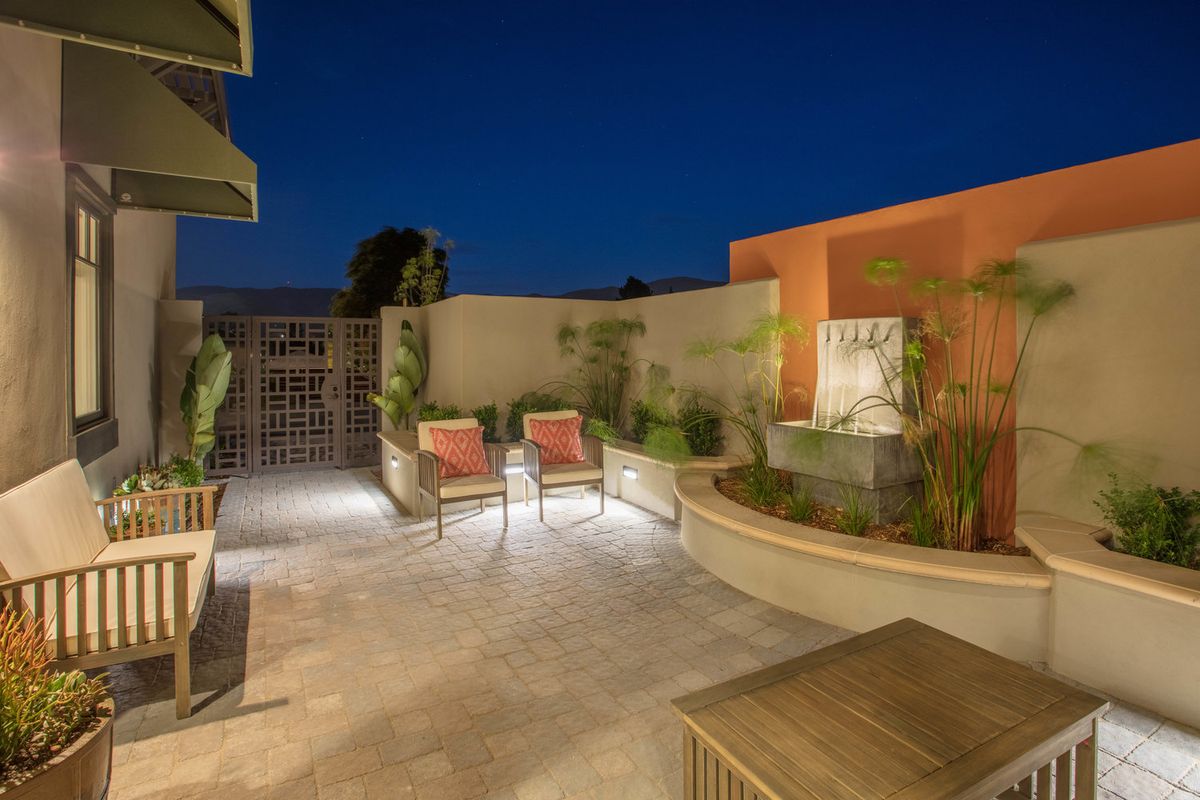 A modern patio at night featuring a stylish seating area and a small fountain, illuminated by soft outdoor lighting.