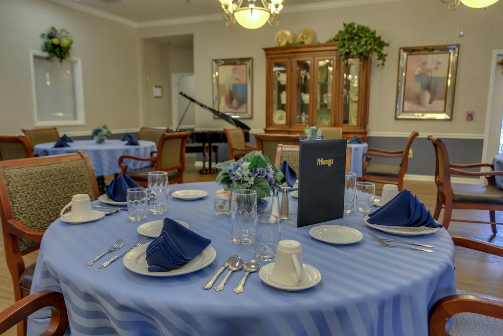 An elegantly set dining room with blue-themed table settings and a piano in the background.