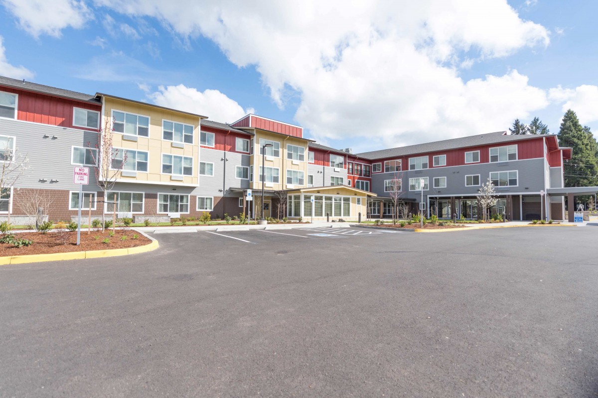 A modern hotel building with a spacious parking lot under a partly cloudy sky.