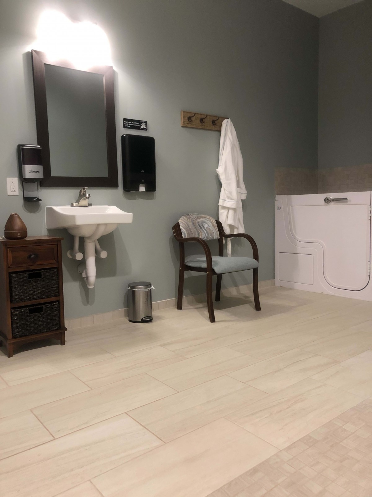 A modern bathroom with a sink, mirror, chair, and laundry appliances.