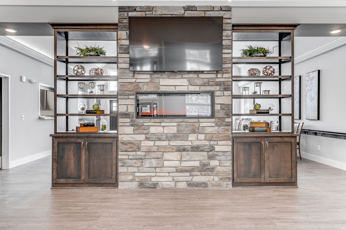 A modern living room with a stone fireplace, built-in shelves, and a large television.