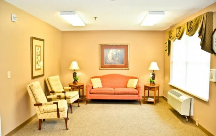 A cozy living room with a pink sofa, two armchairs, side tables with lamps, and a framed painting on the wall.
