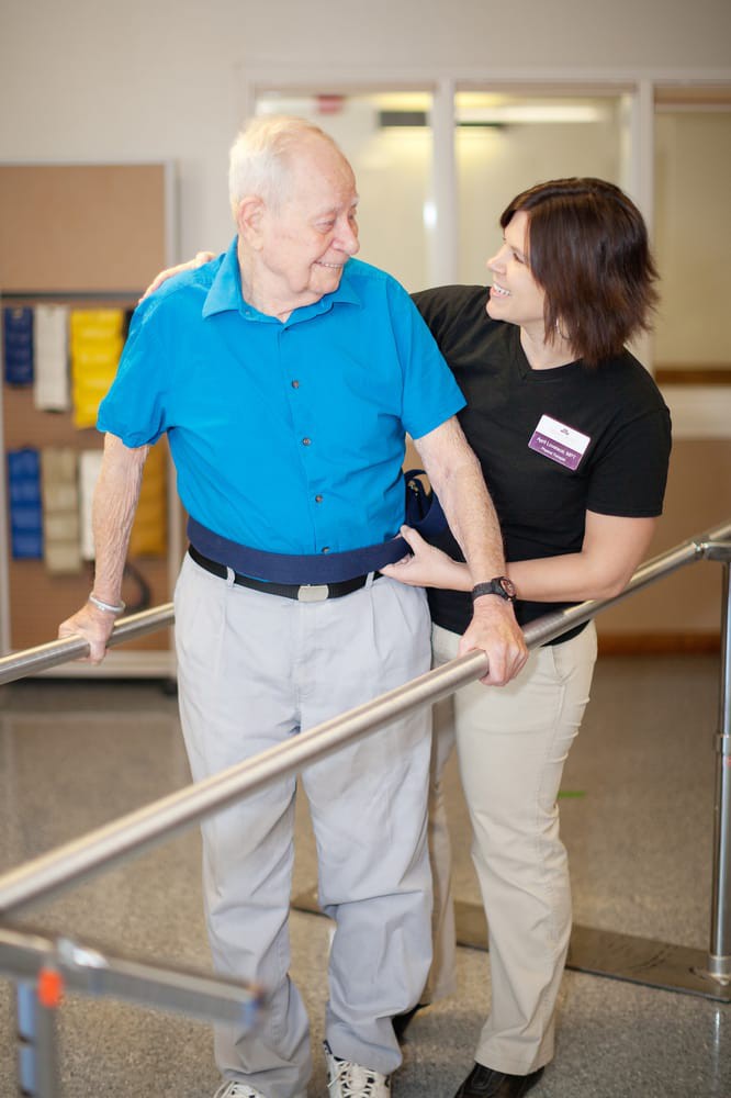 A caregiver assisting an elderly man during a physical therapy session.