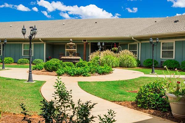 A beautifully landscaped garden with a walkway and fountain in front of a building under a bright blue sky.