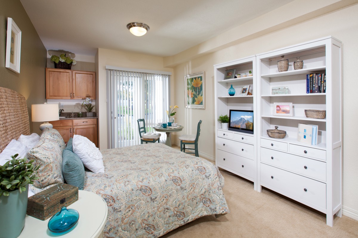 A cozy studio apartment with a bed, small dining table, and built-in shelves.