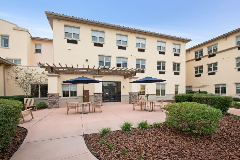 A modern three-story building with a patio area featuring outdoor seating and sunshades.